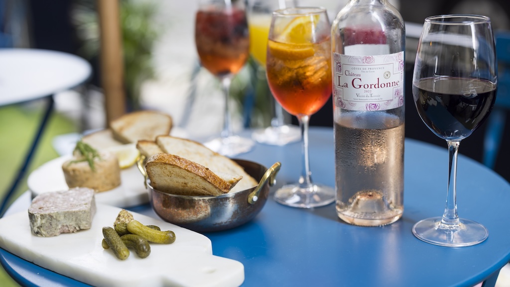 Bread, cornichons, wine and an aperol spritz on a blue outdoor table at La Parisienne.