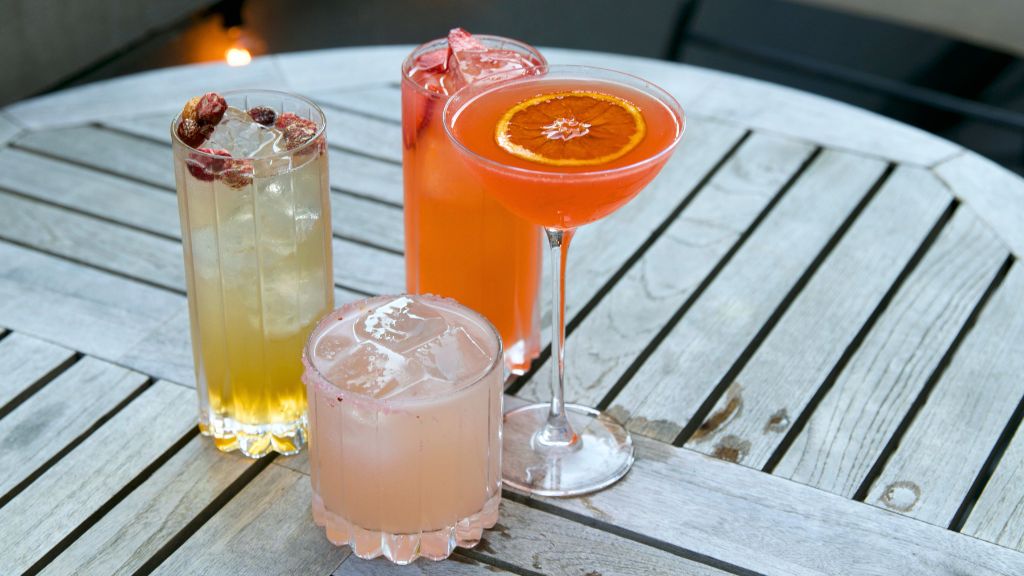 Four colorful cocktails on a wooden table outdoors.