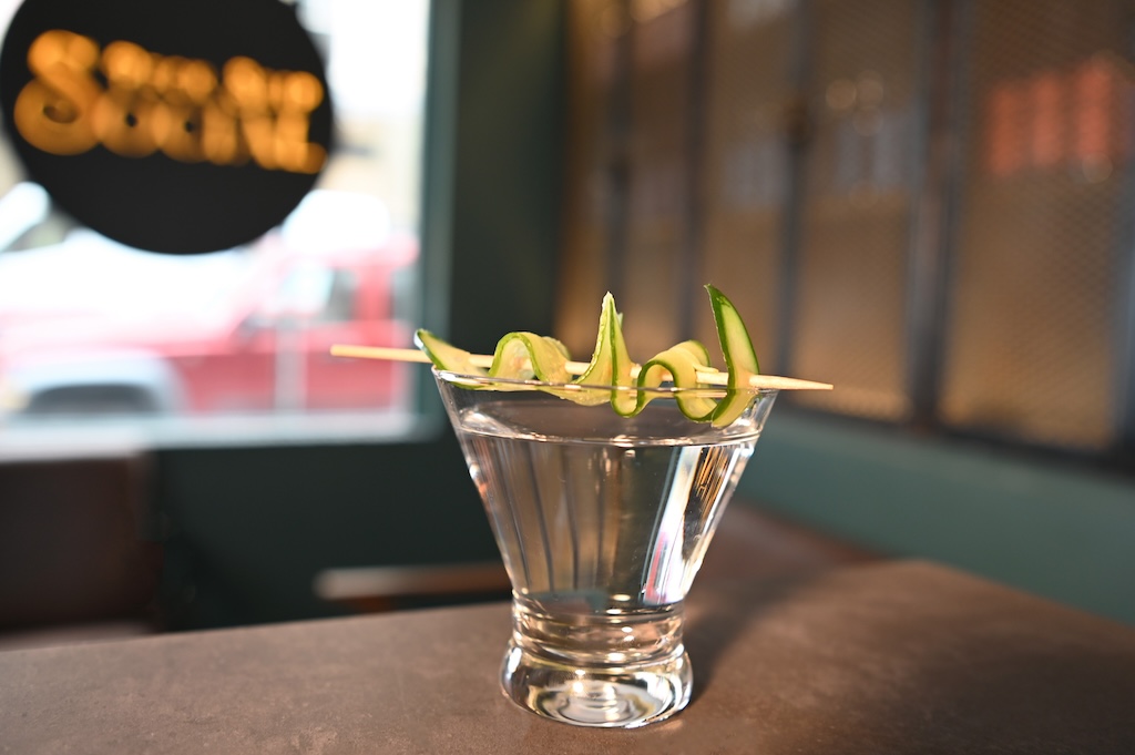 Clear cocktail with pickled cucumber garnish at Peck Slip Social.