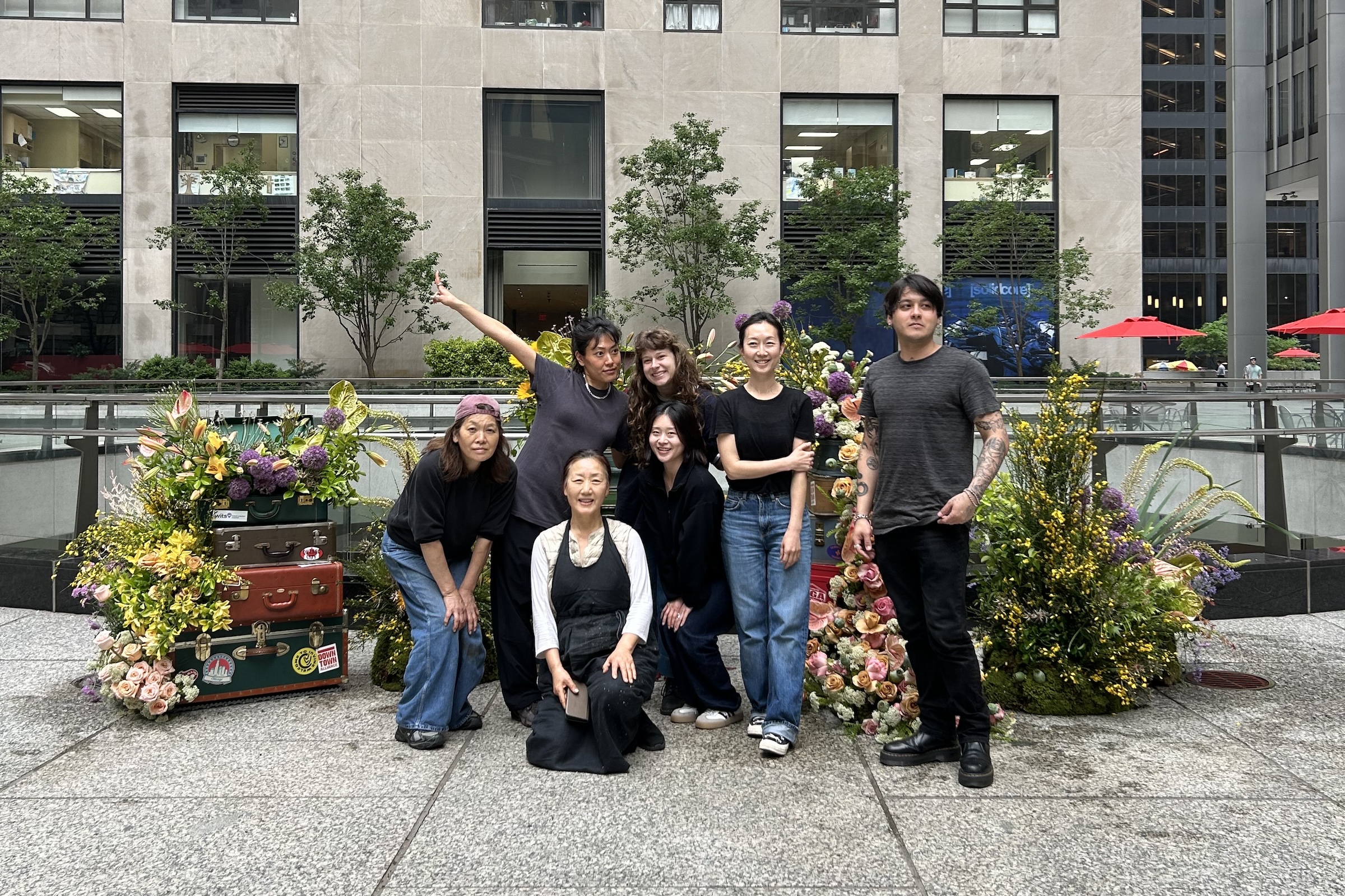 Seven people pose in front of floral display on plaza at 28 Liberty.