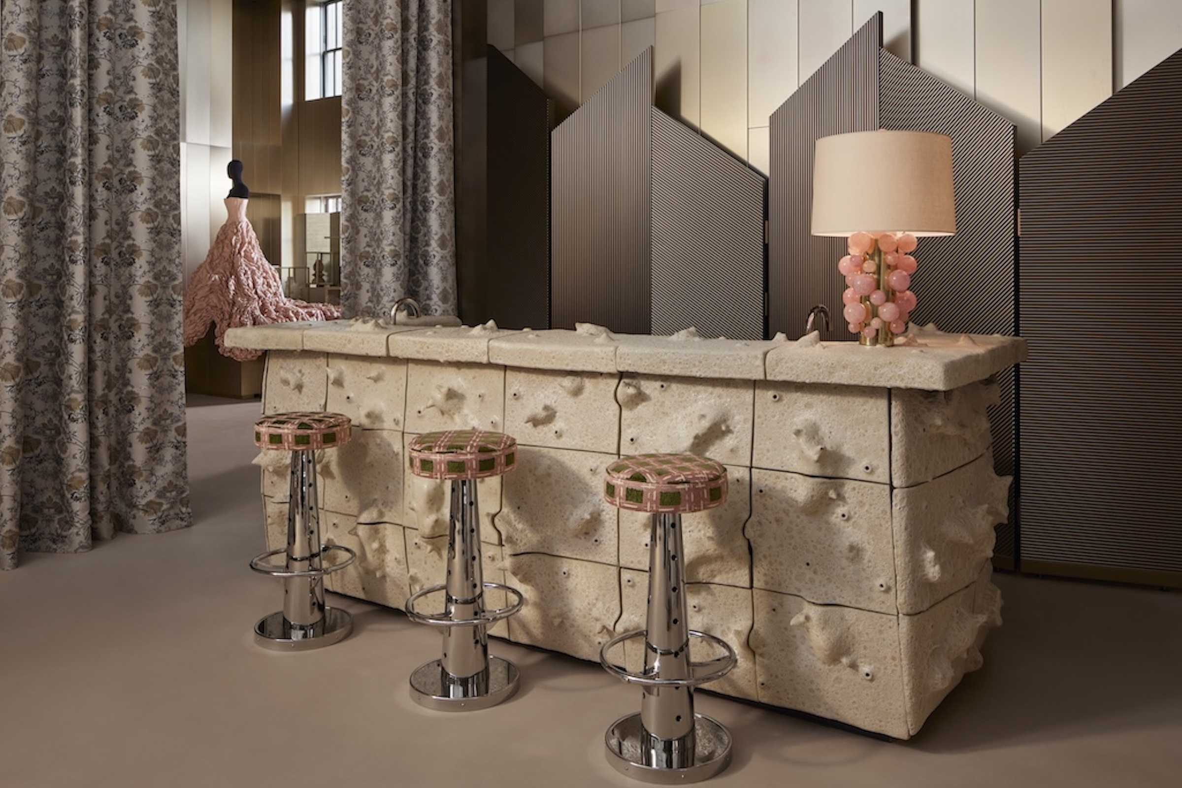A whimsical white bar with pink and silver stools and a pink dress in the background.
