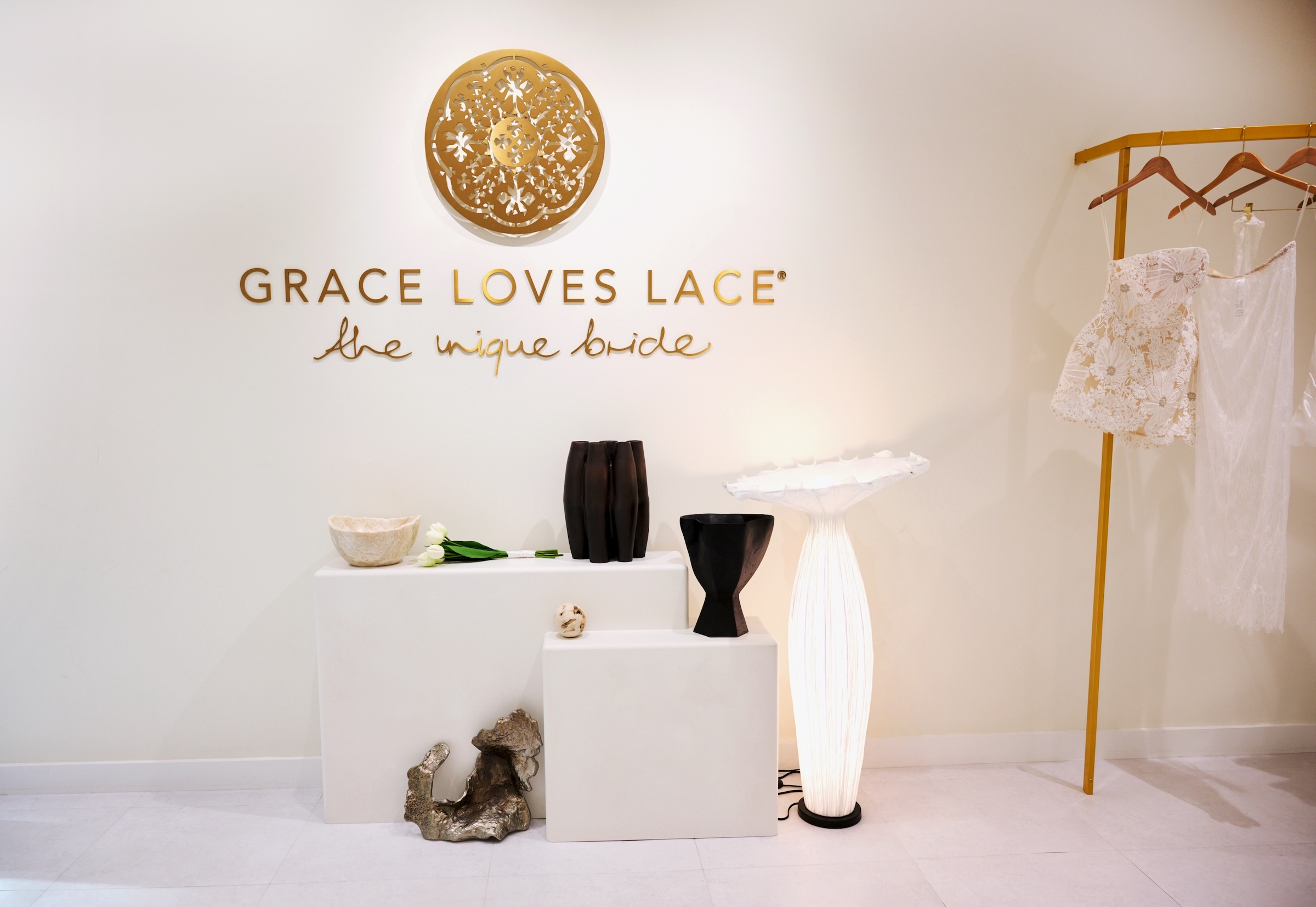 Wedding dress and collection of lights in front of gold sign reading "Grace Loves Lace"