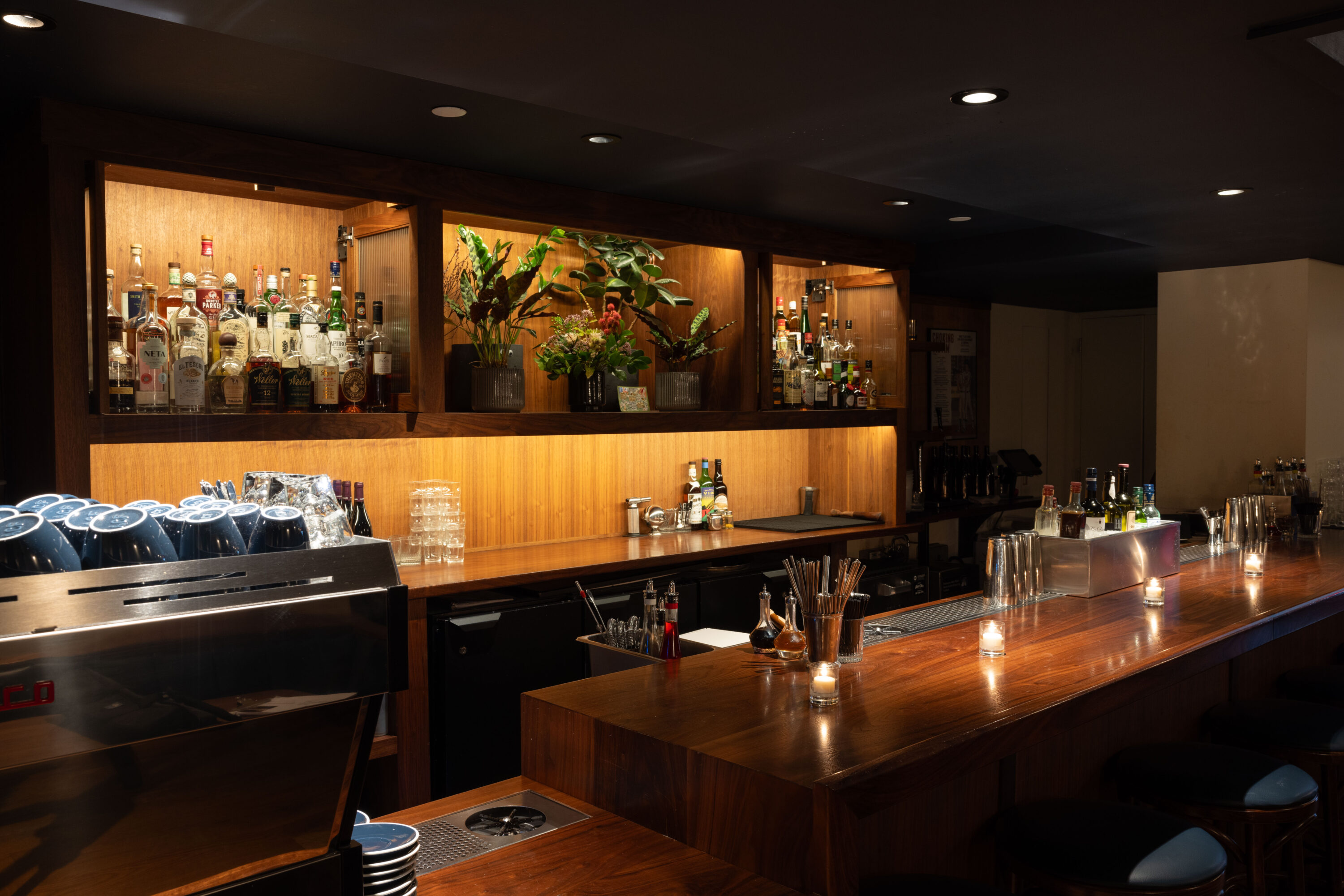 A sleek bar with bottles of alcohol and an espresso machine in view.