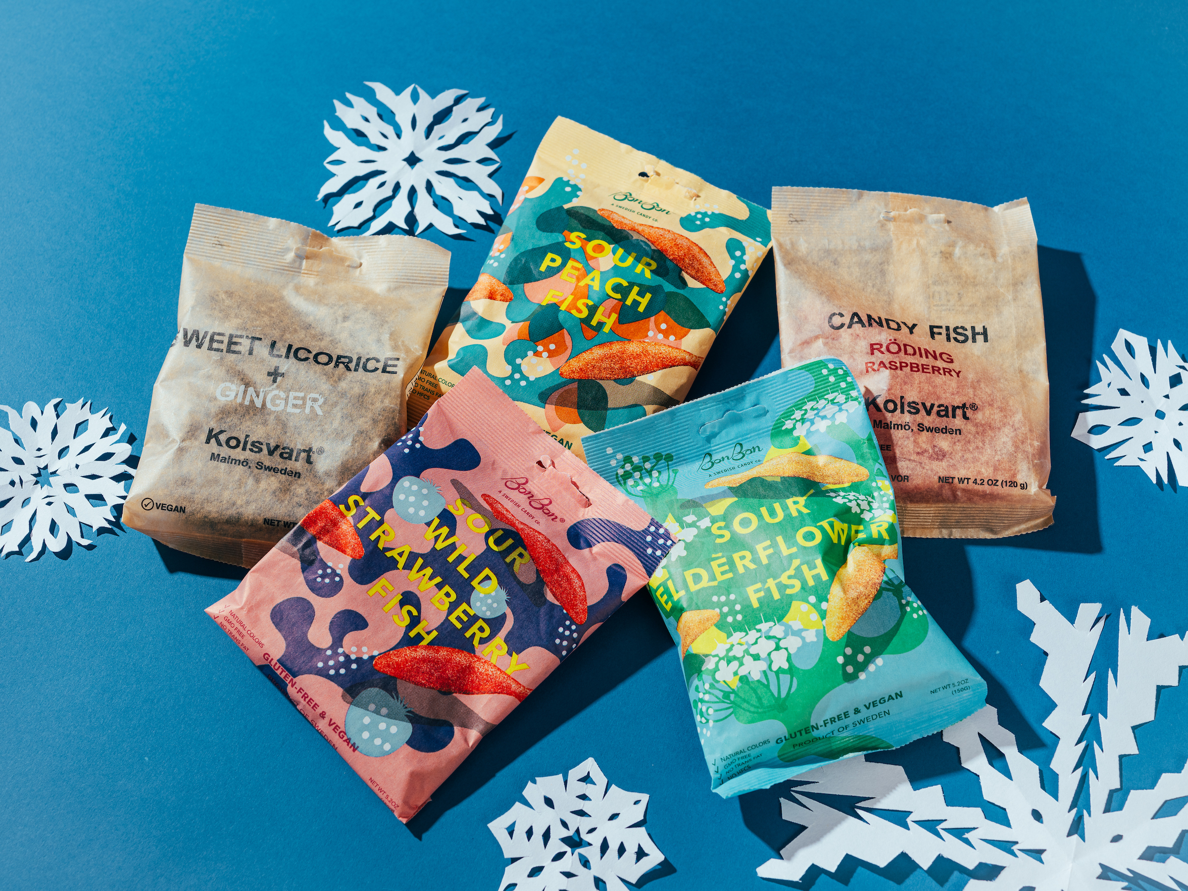 Bags of Swedish candy against blue backdrop with cut-out paper snowflakes.