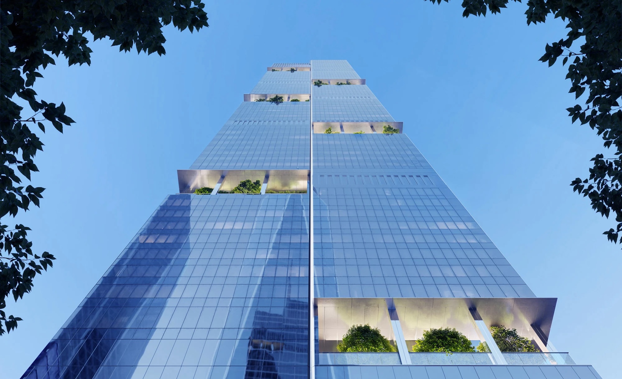 A dramatic low-angle shot looking straight up the side of a glass skyscraper toward a clear blue sky. The building is designed with deep, recessed rectangular cutouts at various levels, each filled with green trees and landscaping to create "hanging gardens." The sleek glass facade reflects the light, and the view is framed by the dark silhouettes of leaves from trees at the ground level.